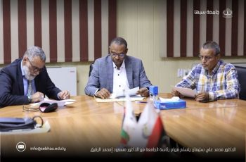 Three men in business attire sit at a conference table reviewing documents, with flags visible in the foreground and an Arabic caption across the bottom.