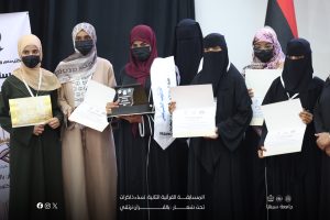 Group of Muslim women in graduation robes and headscarves holding certificates at a ceremony, some wearing masks