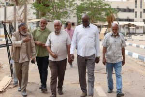Group of men walking together down a sunny street near buildings and palm trees.