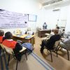 Audience seated in a classroom watching a presenter at a desk, with a large Arabic banner on the wall behind them.