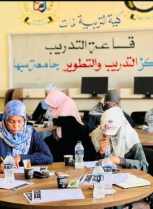 IMG-20261015-WA0009 - جامعة سبها | Sebha University Group of women in hijabs studying at a round table in a classroom, with Arabic signage on the wall behind them.