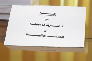 Close-up of a white tilted document with bold Arabic text on a wooden desk.