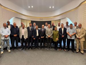 Group of professionals in business attire posing for a formal group photo in a modern conference room.