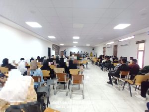 Crowded conference room with a panel of speakers at the front and attendees seated in rows.