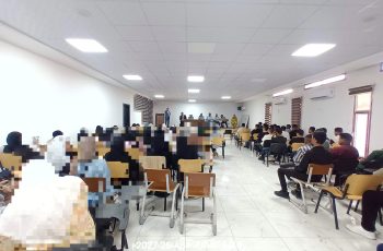 Crowded conference room with a panel of speakers at the front and attendees seated in rows.