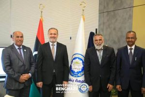 Four men in suits pose for a formal photo in front of Libyan flags and a university banner, at University of Benghazi events.
