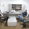 Five men sit around a grey conference desk in a bright office, chatting during a meeting.
