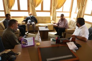 IMG-20261028-WA0017 - جامعة سبها | Sebha University Five men seated in a bright office around beige sofas, discussing documents on a central table.