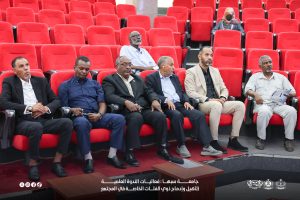 IMG-20261029-WA0009 - جامعة سبها | Sebha University Men in suits and casual attire sit in bright red auditorium seats during a meeting or conference.
