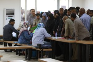 Crowd of people lined up at a service desk while volunteers register them indoors.