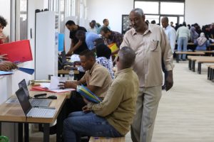 People in a crowded registration area at desks with laptops, filing papers and forms.