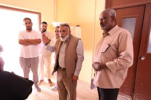 WhatsApp Image 2026-10-12 at 9.47.02 AM - جامعة سبها | Sebha University Five men stand in a doorway hallway, one man in front gesturing as he speaks to the others.