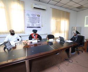 Panel of graduates seated around a long conference table in a classroom, with a large poster on the wall and laptops nearby.