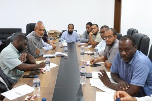 Group of men in a boardroom around a long table, reviewing documents and talking.